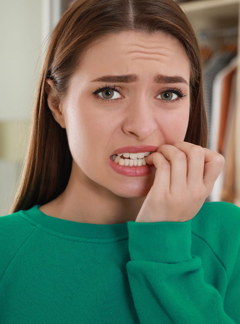 A woman bites her nails with a worried expression