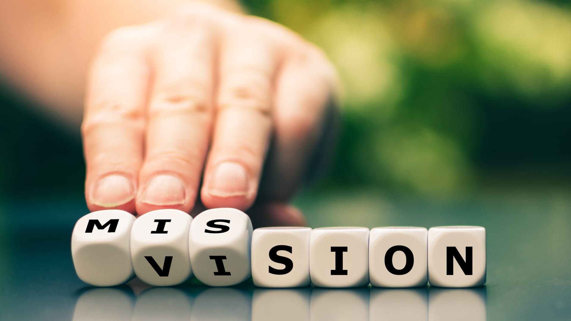 A hand turns a wooden block to change the word "Vision" to "Mission"