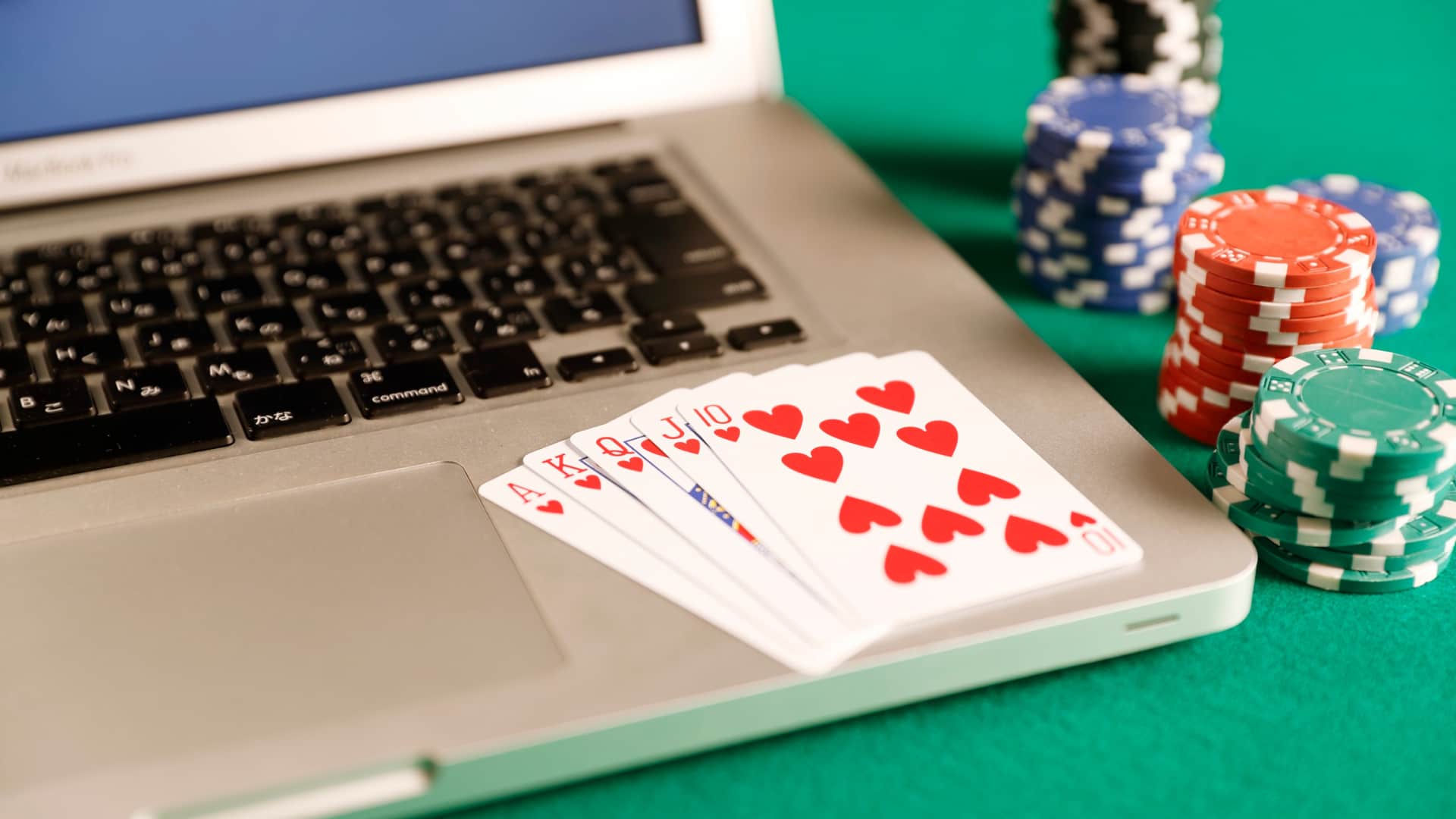 Playing cards and betting chips are next to a laptop