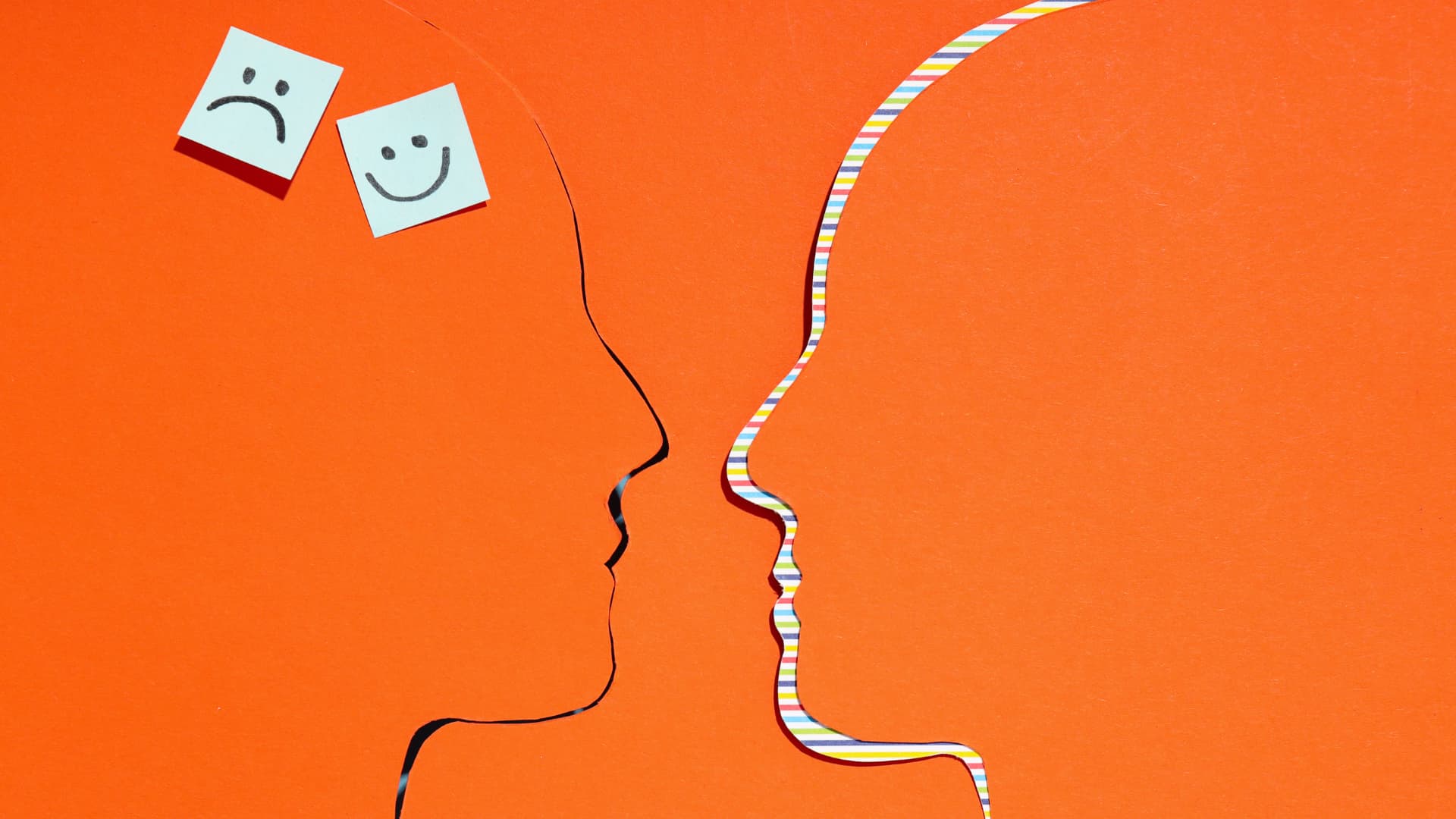 Two head cutouts with conflicting happy and sad face notes