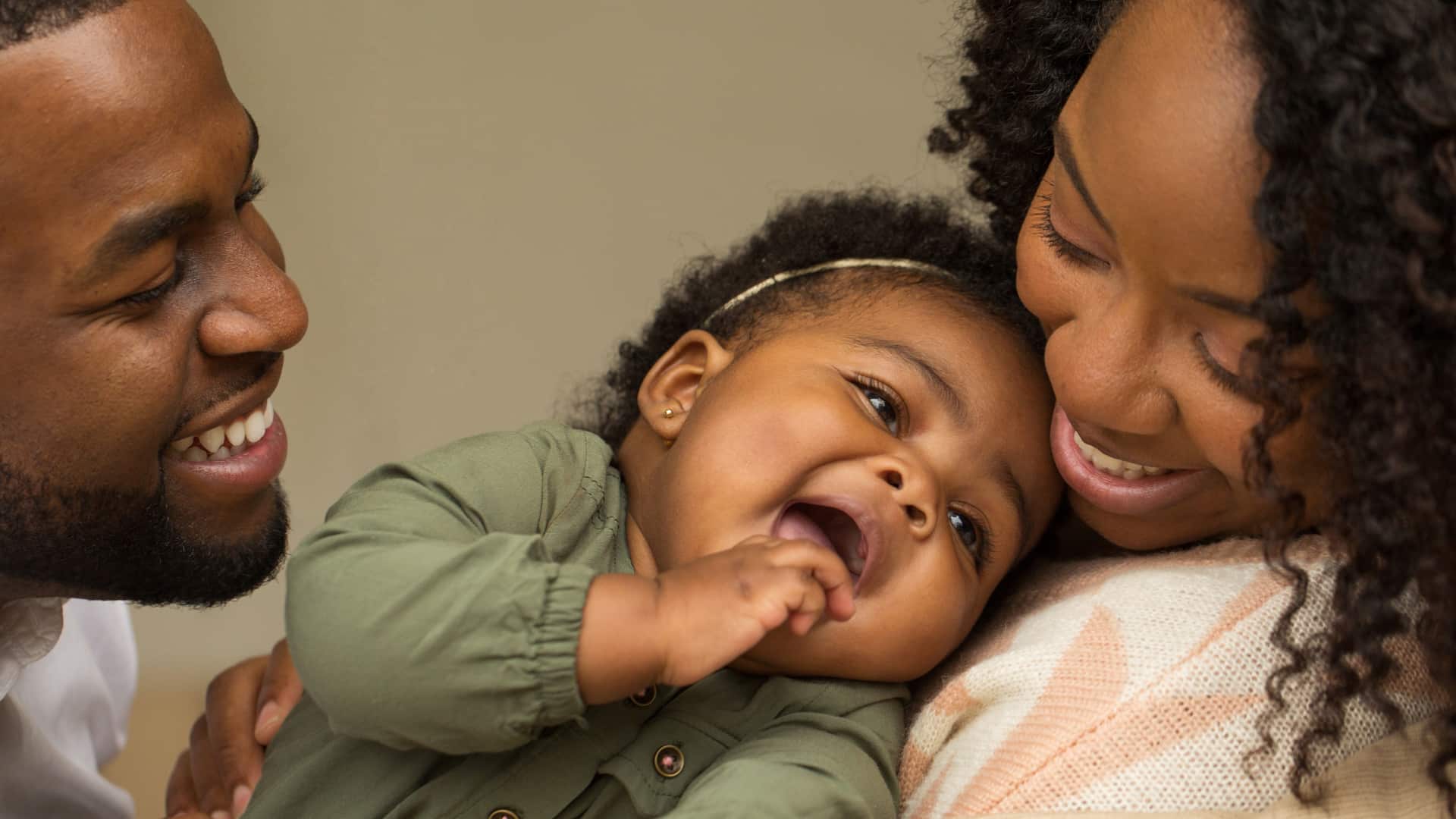 A smiling couple embraces their laughing baby