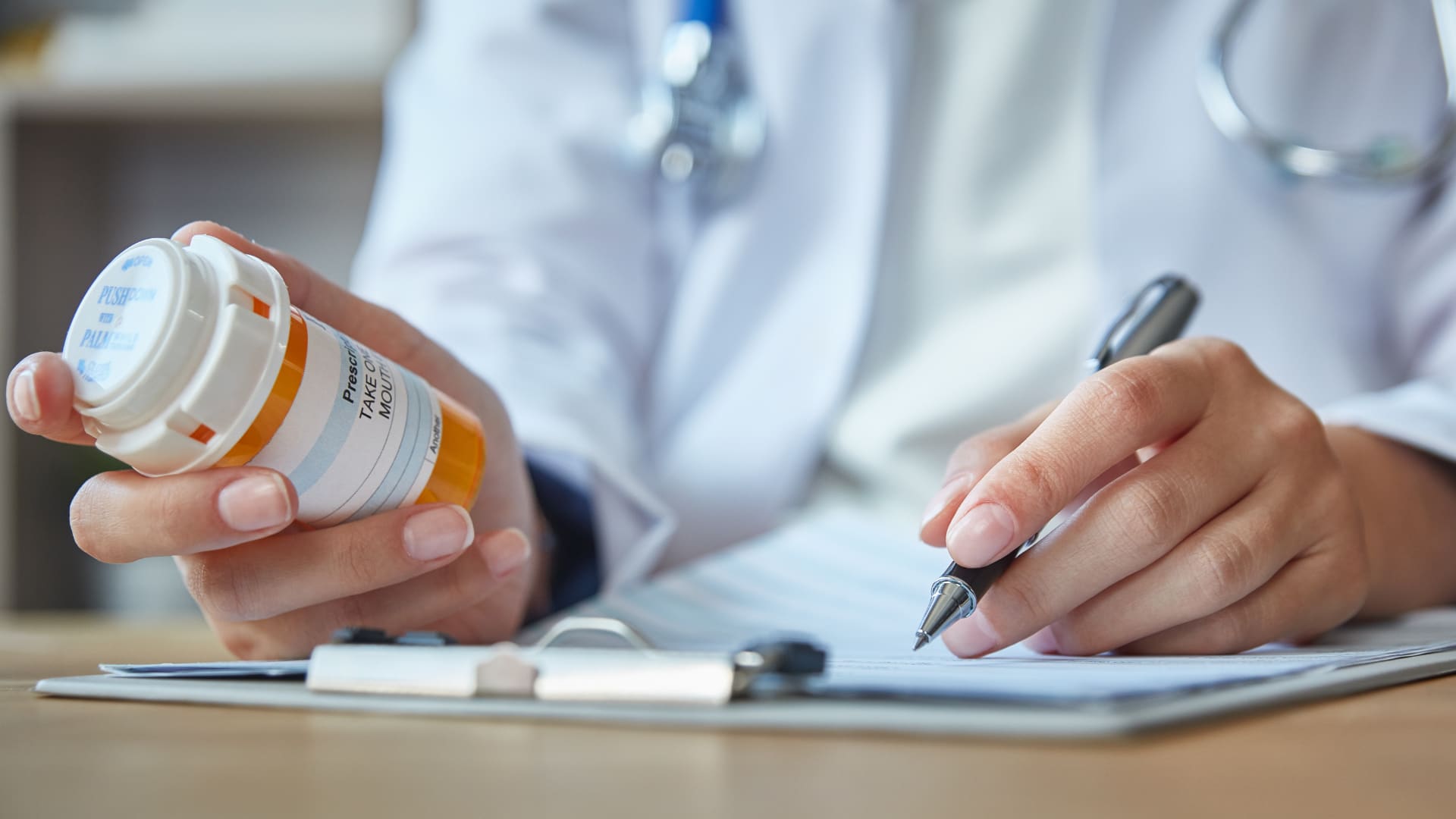 A doctor is holding a prescription bottle and writing