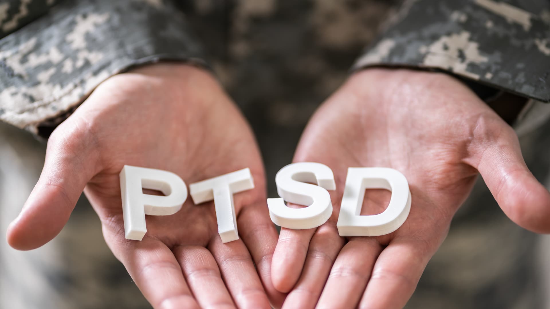 Hands in a military uniform holding the letters "PTSD,"
