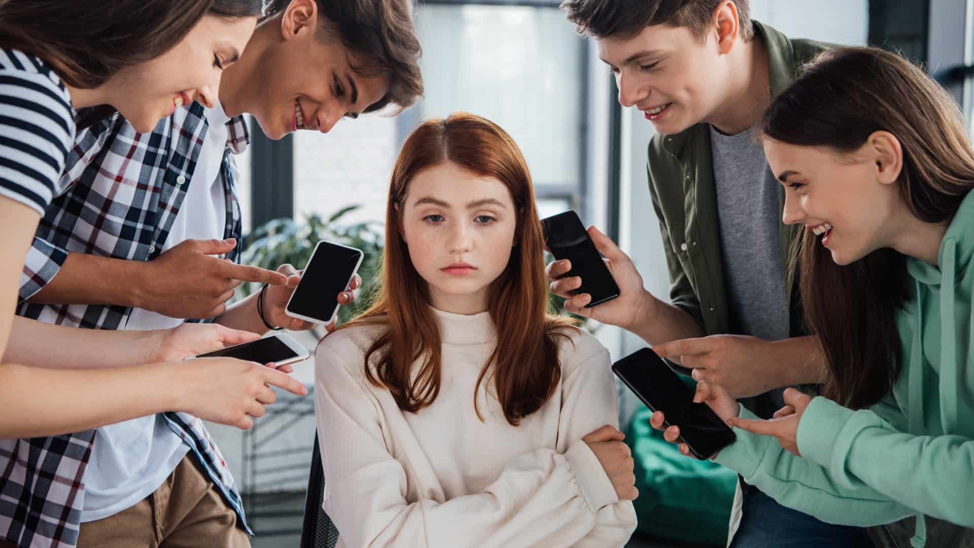 Group of teens pointing phones at one sad girl