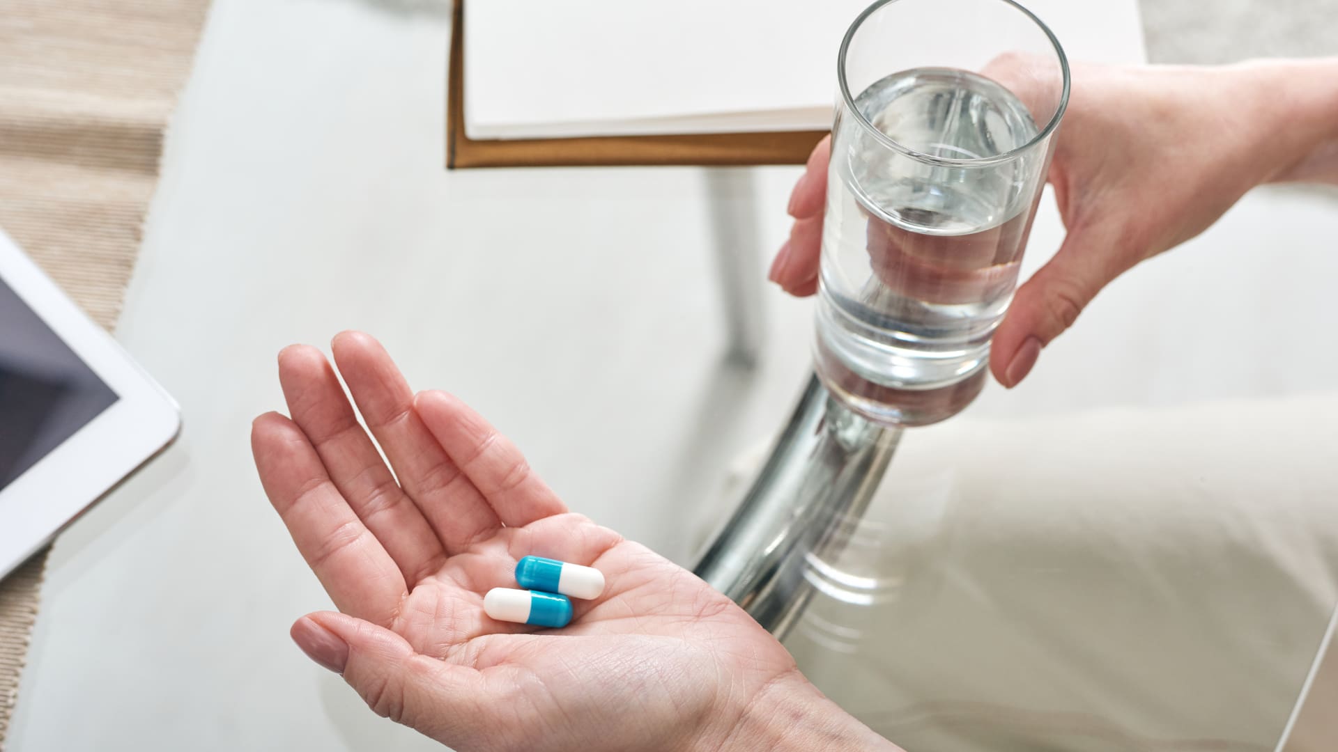 Two pills and a glass of water are held in a hand