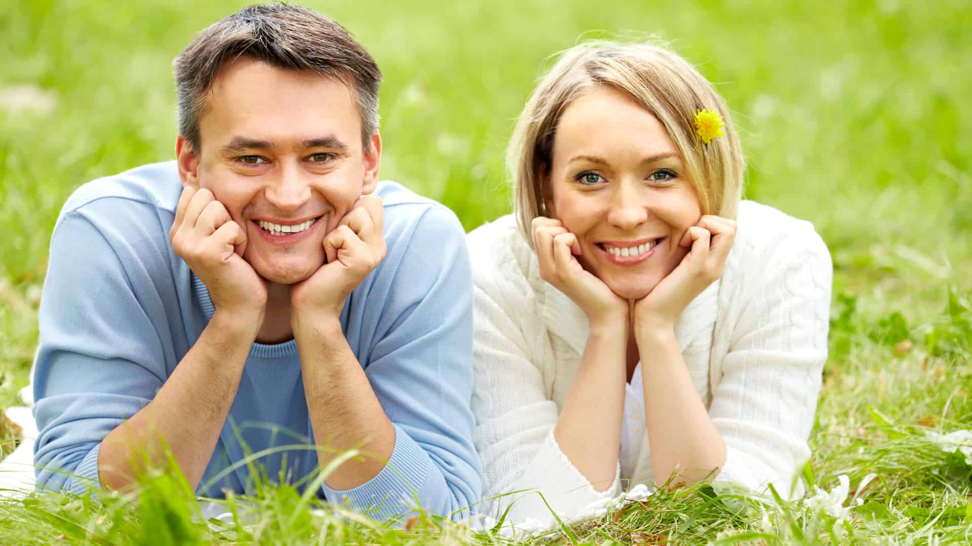 A smiling couple lies happily in the grass