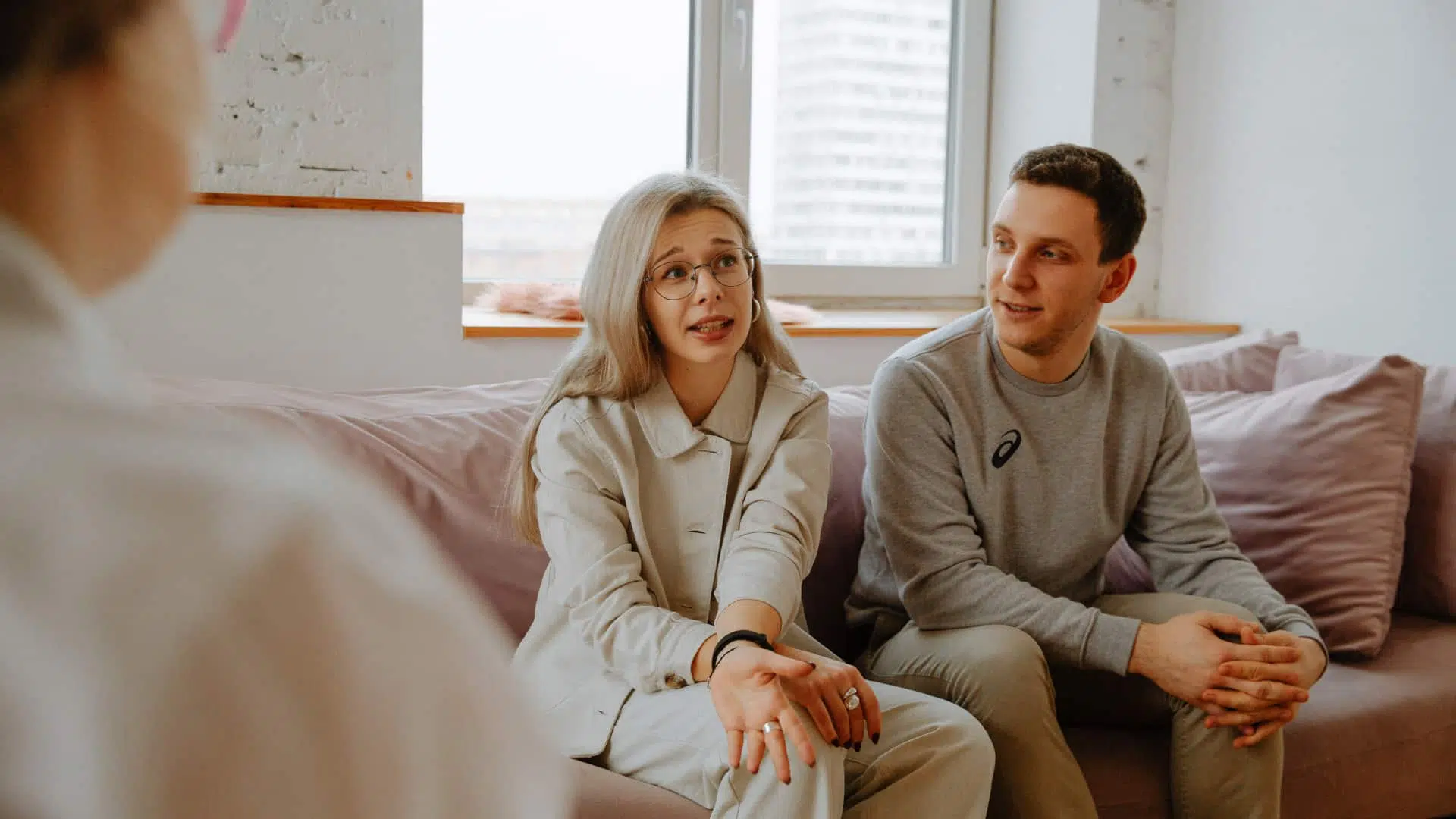 A counselor facilitates an open and supportive dialogue between a young couple on a sofa.