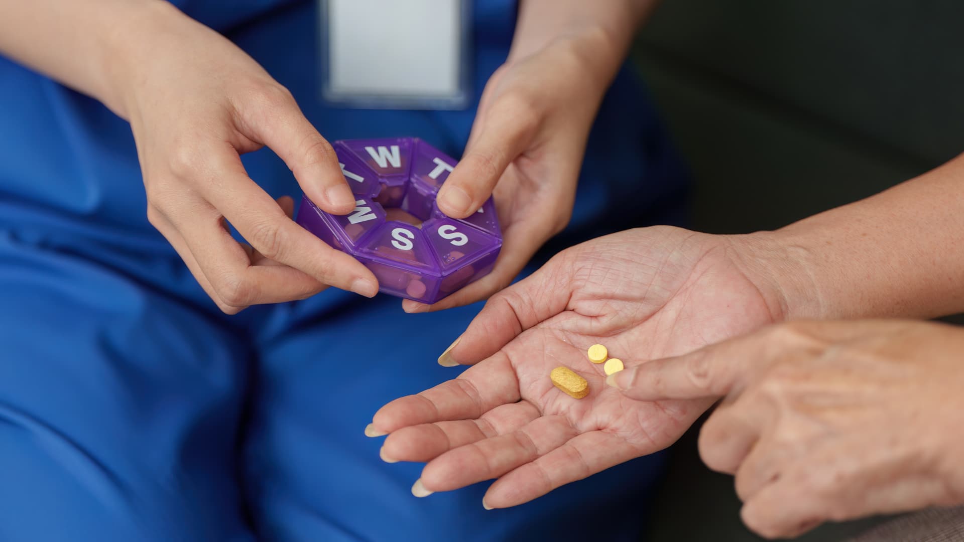 A healthcare provider helps a patient organize and track their daily prescriptions using a pill organizer.