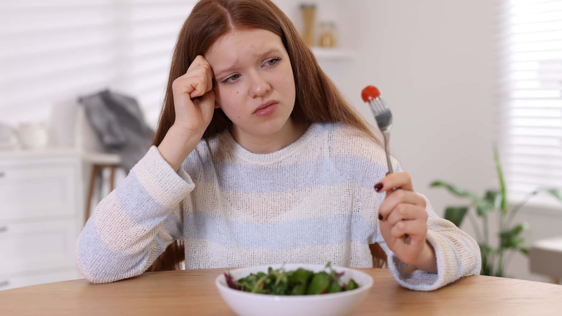 A person sits before a food plate with a single piece of tomato